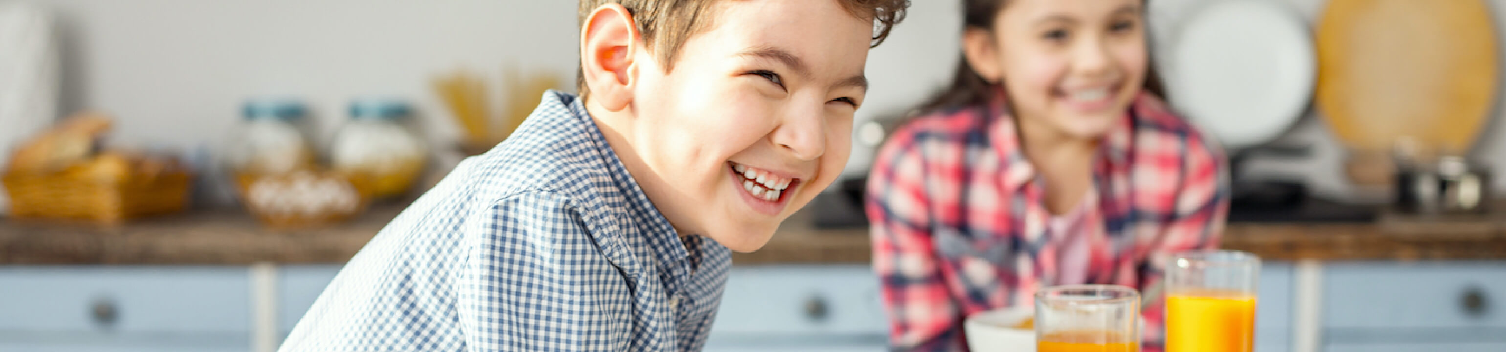 Young boy smiling wide at kitchen table with young girl smiling in background.
